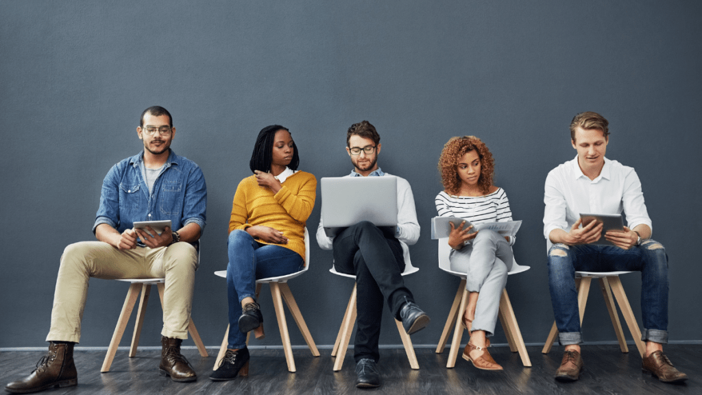 persone sedute con pc, tablet o fogli in attesa di un colloquio