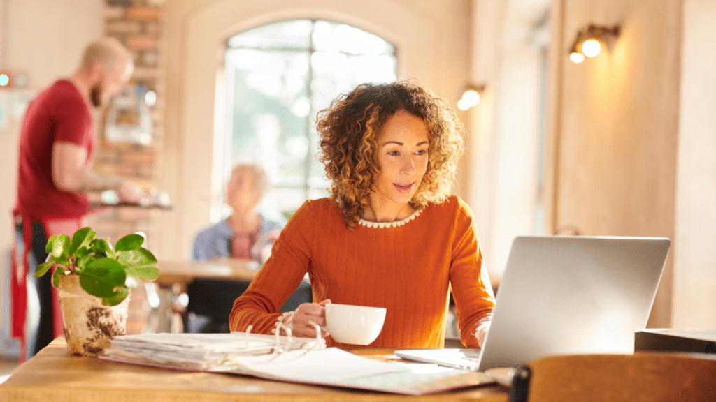 Ragazza con capelli ricci biondi che lavora al computer in un bar grazie alla possibilità di fare remote working