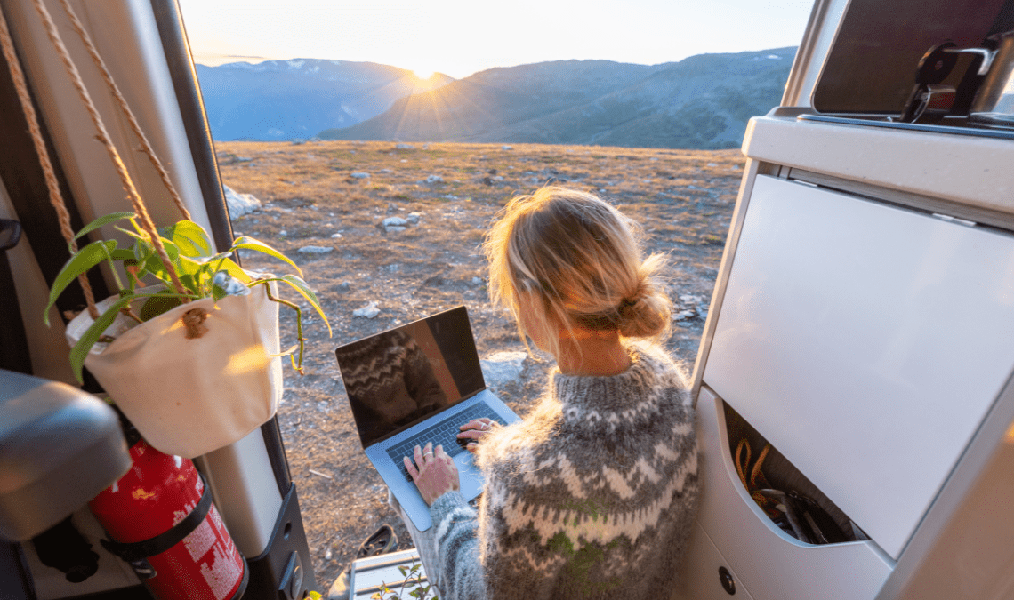 Ragazza bionda che fa remote working dal camper in mezzo alla natura