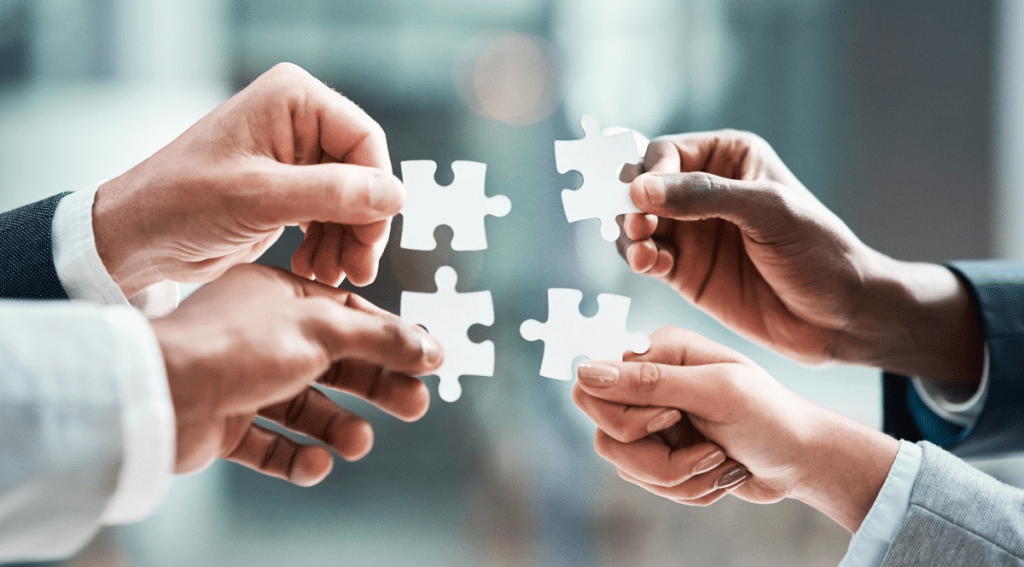 Quattro mani che tengono pezzi di puzzle bianchi, simbolo di collaborazione e lavoro di squadra.