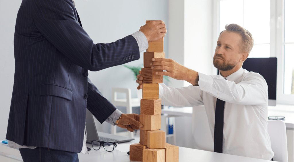 Seri uomini d’affari di età diverse costruiscono una torre di blocchi nell’ufficio dell’azienda come metafora della successione aziendale e della collaborazione. Concetto di gestione del rischio e mantenimento della stabilità finanziaria.