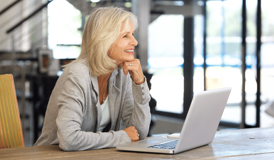 Ritratto di una donna anziana sorridente che lavora al computer portatile in ambienti interni.