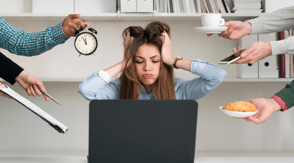 Donna stressata davanti al computer in ufficio, circondata da colleghi che le porgono oggetti diversi — un orologio, una tazza di caffè, un telefono e documenti — simbolo di sovraccarico di lavoro e multitasking.