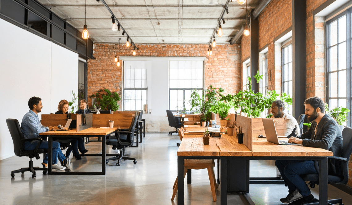 Ufficio moderno con open space luminoso, arredi in legno, piante e professionisti al lavoro in un ambiente collaborativo ed efficiente.