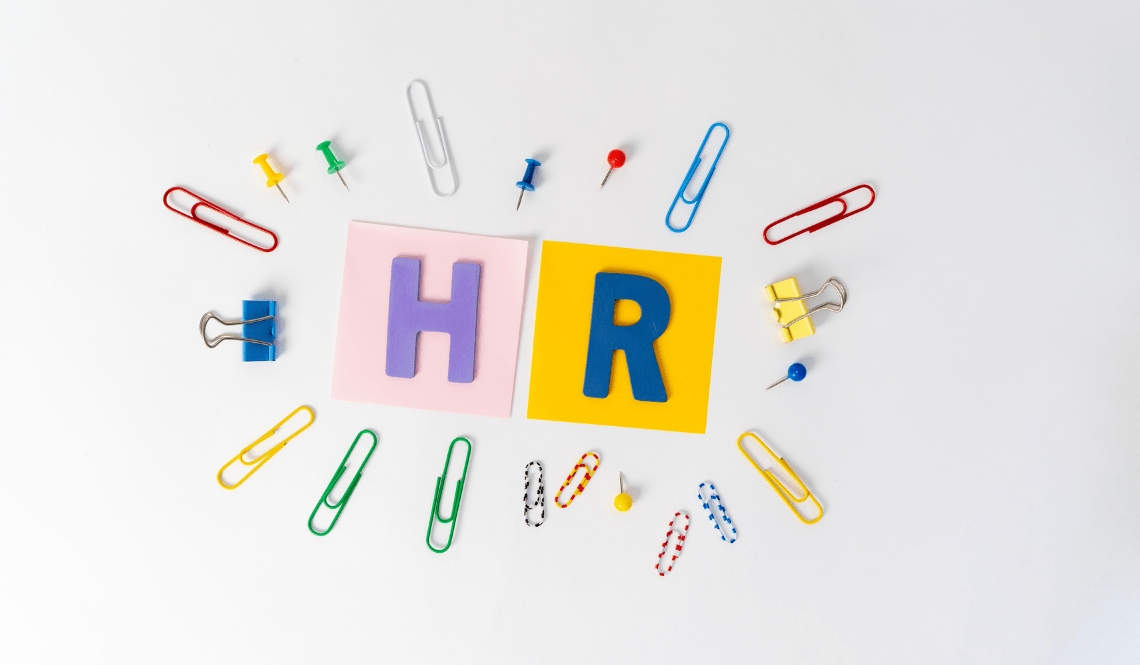 Lettere HR su sfondo bianco con graffette colorate, simbolo delle risorse umane e del loro ruolo organizzativo.