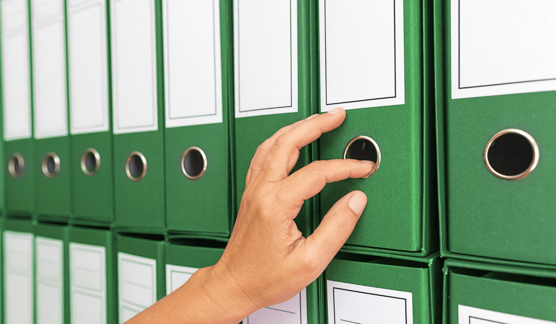 Mano che prende un raccoglitore da archivio, simbolo di organizzazione, chiarezza di ruoli e accountability nei team di lavoro.