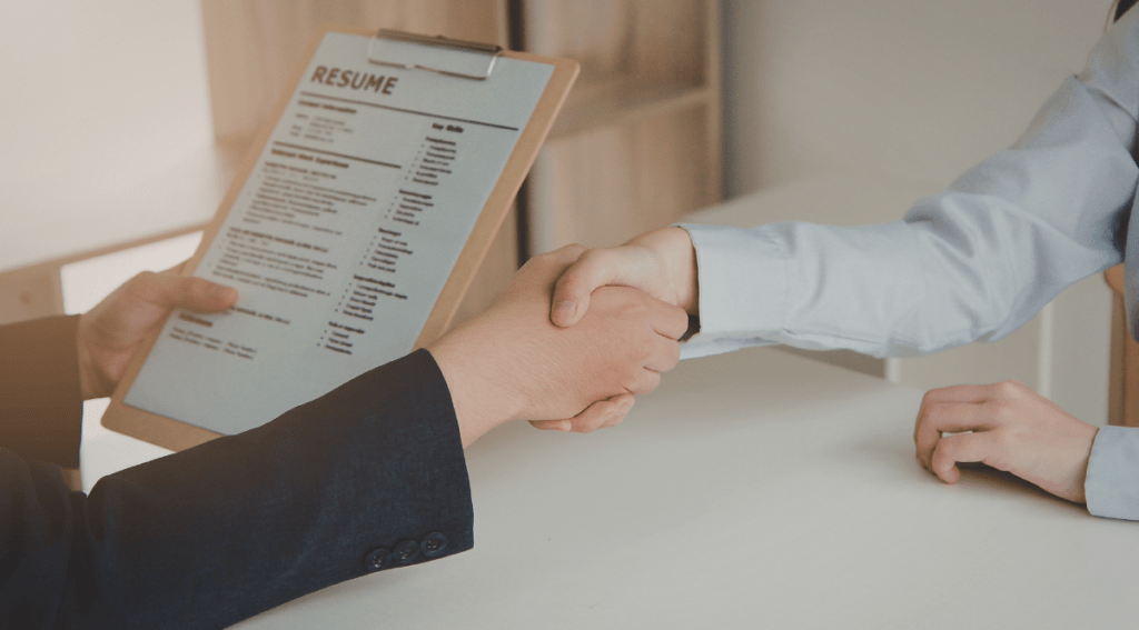 Stretta di mano durante un colloquio di lavoro con curriculum in evidenza, simbolo di valorizzazione delle competenze professionali.